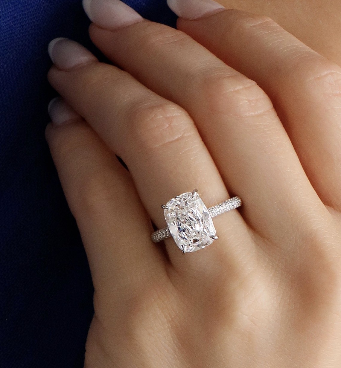 A close-up of a woman’s oval engagement ring with a textured silver band on her ring finger.