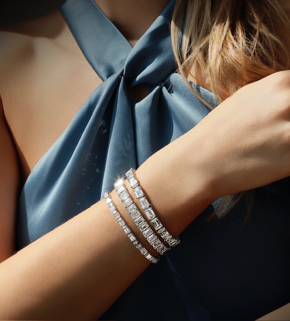 A close-up of an elegantly dressed woman’s wrist, adorned with 3 tennis bracelets with emerald cut diamonds. A close-up of an elegantly dressed woman’s wrist, adorned with 3 tennis bracelets with emerald cut diamonds.