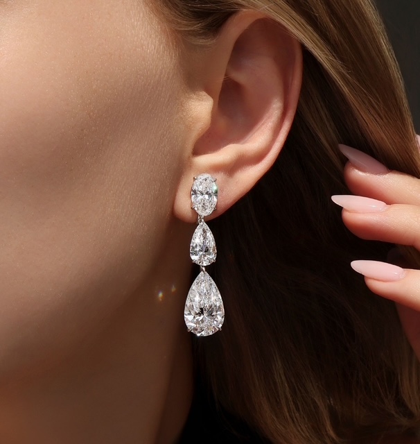 A close-up of a young woman’s ear wearing a stunning drop earring featuring oval and pear cut diamonds. A close-up of a young woman’s ear wearing a stunning drop earring featuring oval and pear cut diamonds.