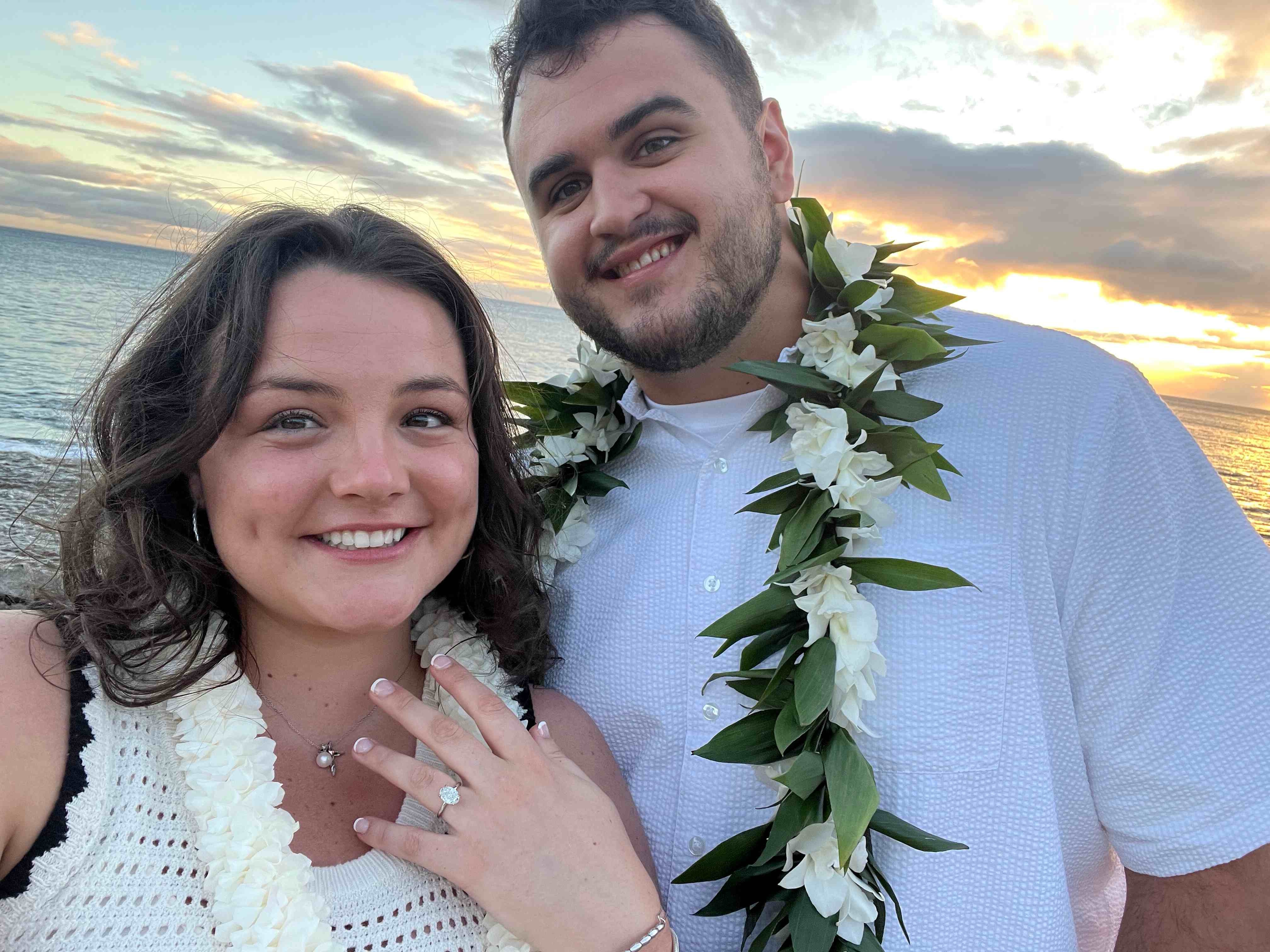 Julie and Matthew taking a selfie on a beach at sunset wearing leis