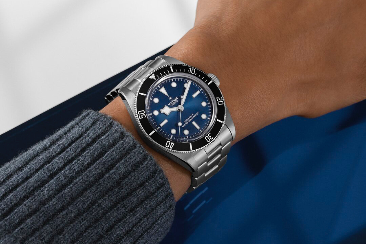 A close-up of a man’s wrist, clad in a stainless steel TUDOR watch with a blue dial.