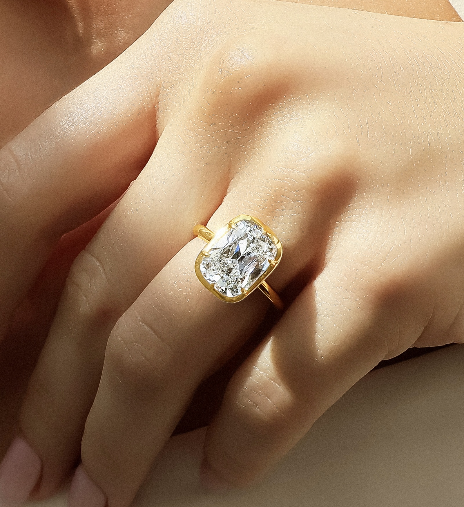 A close-up image of a yellow gold bezel engagement ring on a well-manicured hand.